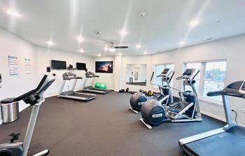 A spacious gym with various exercise equipment and a flat screen TV mounted on the wall.